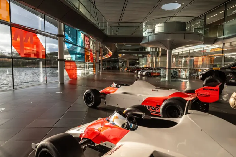 Red-and-white McLaren Formula 1 cars in the foreground of the McLaren Technology Centre