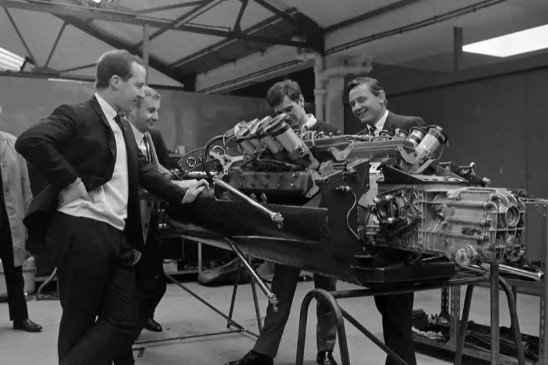 Black-and-white photo of McLaren engineers working on an engine and chassis in the workshop