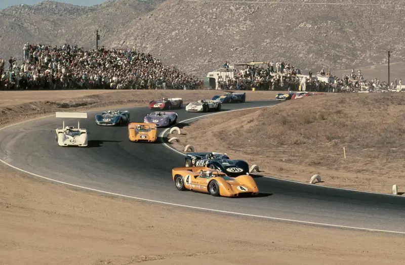 Papaya McLaren Can-Am cars leading the field through a hillside corner
