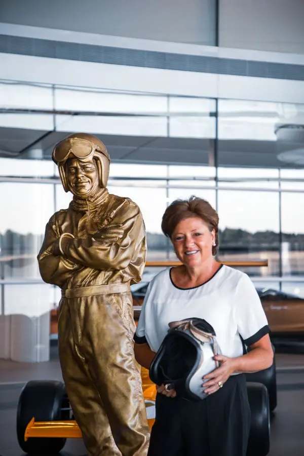 Amanda McLaren holding a vintage racing helmet beside a statue of her father