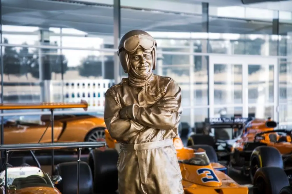 A statue of Bruce McLaren in racing overalls among McLaren race cars