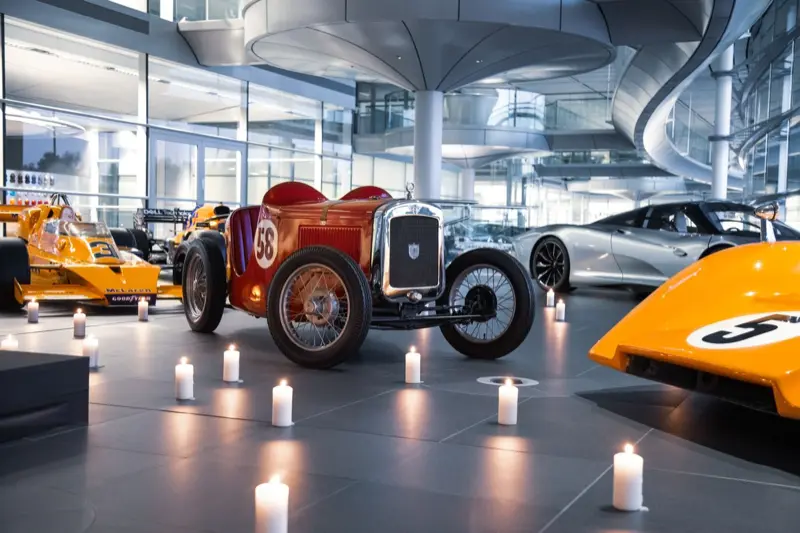 Bruce McLaren’s red Austin 7 Ulster displayed by candlelight among papaya McLaren race cars