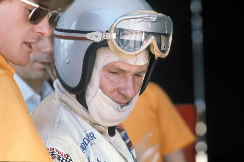 Bruce McLaren in his helmet and goggles, with team members in papaya shirts beside him